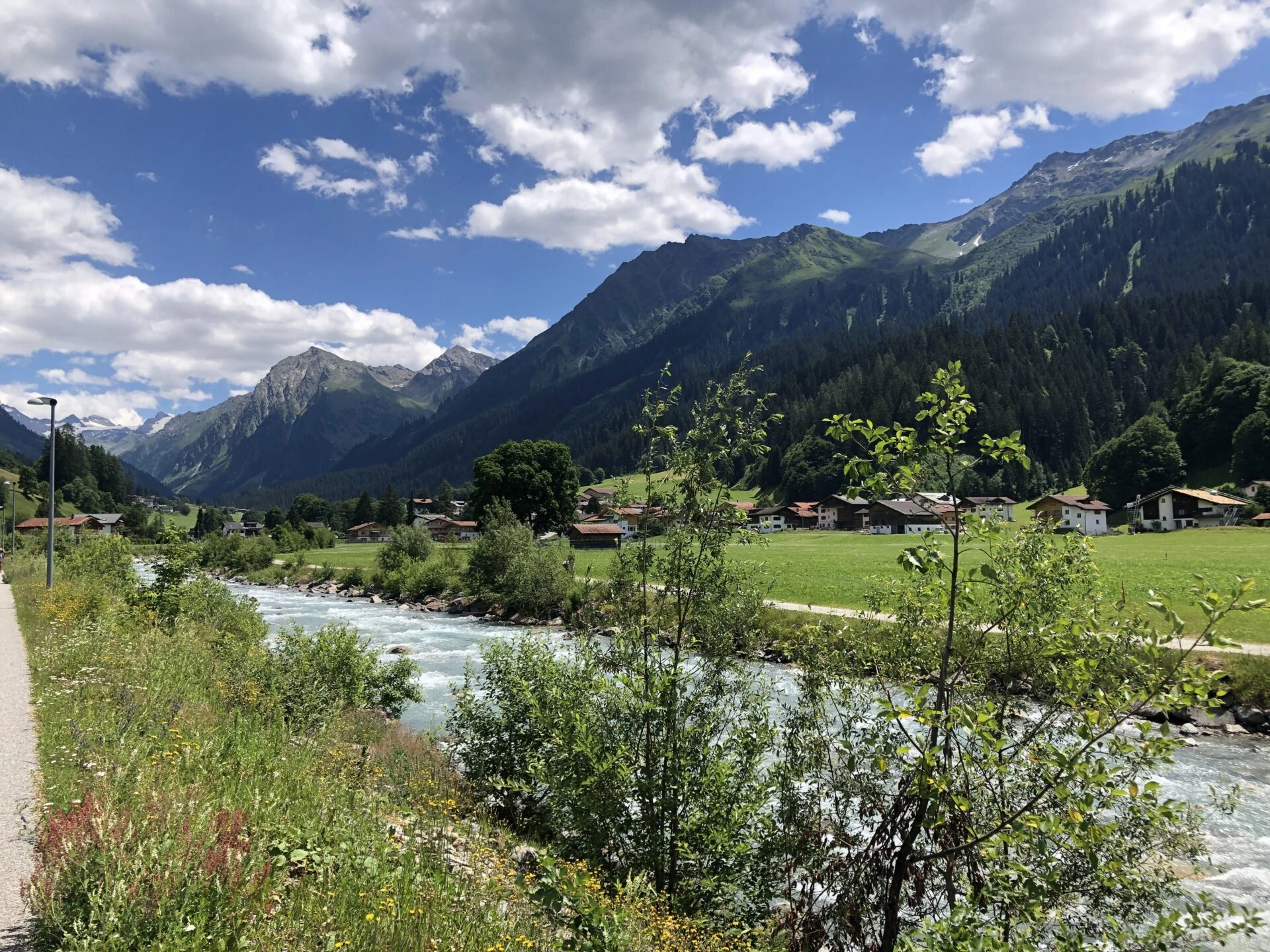 Sommerlandschaft Klosters mit Fluss, grünen Wiesen und Alpen unter blauem Himmel